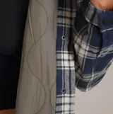 Campera tipo sobrecamisa de corte cropped, confeccionada en tela de franela con diseño de cuadros en tonos azul marino y crema. Presenta cuello clásico, cierre frontal con botones, bolsillos con solapa en el pecho y forro interior acolchado.