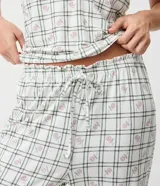 Pijama largo de dos piezas confeccionado en tejido peach touch, con estampado de cuadros y pequeños detalles florales. Incluye una blusa de manga corta con escote en V, frunce en el busto y bordes ondulados, y un pantalón de corte recto con cintura elástica y cordón ajustable.