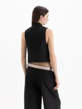 Chaleco Capri de corte cropped y calce al cuerpo, confeccionado en tejido color negro. Presenta escote redondo pronunciado con detalle de volados tableados que recorren el contorno y cierre cruzado delantero con seis botones metálicos. Incluye bolsillos frontales ojal.