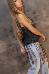 Top tejido a crochet en color dorado con destellos brillantes, de escote redondo y sin mangas. Presenta un diseño de flecos largos en la parte inferior en tonos rojo y dorado.