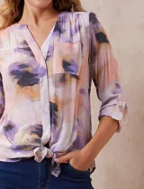 Blusa estampada de Zac & Rachel con cuello a la base, escote en V y botones. Tiene un bolsillo aplicado en la parte delantera, mangas largas regulables con presilla y botón, y terminación anudada opcional.