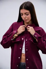 Sobrecamisa de gamuza en color violeta, con diseño de corte holgado, cuello camisero clásico, cierre frontal con botones metálicos a presión y dos bolsillos frontales tipo parche.