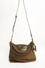Cartera tipo shopper color marrón, con solapa frontal decorativa en tono más oscuro y tiras con nudos. Incluye herrajes dorados y un charm colgante con cuentas de madera.