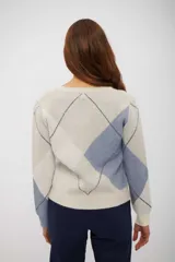 Sweater de punto con cuello en V y diseño de rombos en tonos beige, azul y blanco. Presenta mangas largas con puños ajustados y corte clásico.