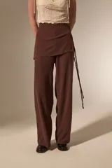 Pantalon de corte recto y tiro alto, confeccionado en tela texturizada color marrón, con detalle de falda superpuesta en la cintura.