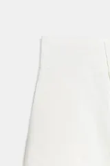 Pantalón balloon de tiro alto color blanco con pliegues en la parte delantera, bolsillos laterales ocultos y cierre frontal con cremallera, botón interior y ganchos metálicos.