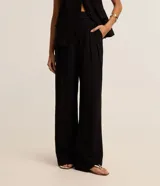 Pantalón de vestir negro, corte pantalona ancho y fluido, con pliegues frontales y cierre de botón en la cintura.