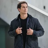 Chaqueta negra acolchada con diseño de rombos, cuello de pana y cierre frontal con botones a presión.