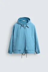 Cazadora técnica ligera de corte regular, con capucha ajustable, cierre frontal con cremallera y puños elásticos. Presenta bolsillos tipo plastrón en la parte frontal y bajo ajustable con cordón.