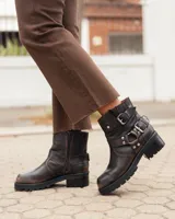 Botas de cuero estilo biker en color marrón oscuro con efecto desgastado. Presentan un diseño de caña corta con correas ajustables con hebillas metálicas y detalles de remaches. Cuentan con una suela de goma dentada y tacón bajo.