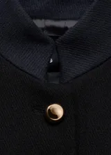 Chaqueta negra de estilo militar entallada, con cuello mao, cierre frontal de botones dorados con efecto joya y manga larga con trabillas y puños abotonados.