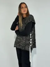 Chaleco de punto color beige con diseño trenzado, sin mangas y con lazos laterales.