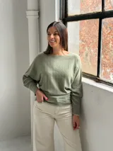 Sweater de punto color verde oliva, con cuello bote y mangas murciélago. Presenta un diseño de textura acanalada vertical en el frente y puños ajustados.