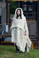 Poncho tejido a mano en lana merino color crudo, con capucha, cuello alto y flecos.