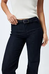 Jean negro de calce flare con cinturón incorporado en la misma tela y silueta ajustada en cadera que se ensancha hacia el ruedo.