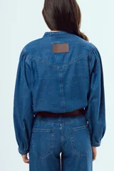 Camisa de denim azul oscuro con cuello mao, mangas abullonadas con puños elastizados y cierre frontal de botones metálicos.