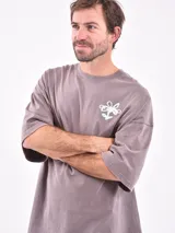 Remera de manga corta color gris claro, corte oversize, con cuello redondo y un pequeño estampado en el pecho con texto en color verde.