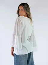 Blusa de algodón color gris oscuro con efecto gastado, mangas largas amplias con múltiples volados escalonados y terminaciones deshilachadas.
