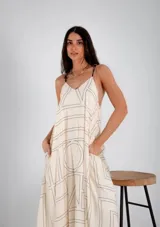 Vestido largo confeccionado en viscosa color crudo, con estampado geométrico lineal en tonos negros, escote en V, breteles finos ajustables y bolsillos laterales.