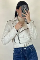 Chaqueta corta tipo biker confeccionada en gamuza color beige, con cierre frontal cruzado, solapas amplias, bolsillos con cierre y cinturón ajustable en la cintura.