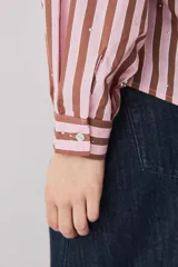 Camisa a rayas verticales en tonos rosado y marrón, de manga larga abullonada, cuello camisero y cierre frontal de botones con pequeños apliques brillantes.