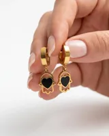 Caravanas tipo argolla con dije colgante en forma de mano de Fátima con un corazón negro en el centro, confeccionadas en acero dorado.