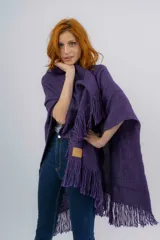 Ruana artesanal tejida en telar manual, color violeta, con textura rústica y terminaciones con flecos en los bordes. Incluye etiqueta de cuero con la marca Pura Lana.