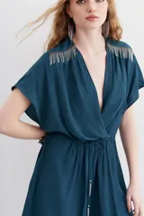 Vestido mini de escote cruzado en color azul petróleo, con mangas cortas y cintura elastizada con lazo ajustable. Presenta detalles de cadenitas metálicas decorativas en los hombros y en la terminación del lazo.