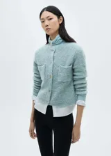 Chaqueta de punto bouclé color celeste, con cuello redondo, cierre frontal de botones joya y dos bolsillos de parche delanteros.