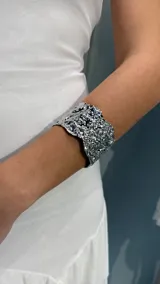 Brazalete rígido de metal plateado con una superficie irregular y texturizada que simula metal fundido.