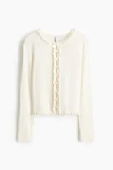 Saco ajustado de punto acanalado fino marca H&M Divided, color blanco, con cuello redondo y cierre frontal de botones. Presenta ribetes de volados en el escote, la tapeta y el bajo.