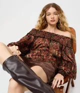 Blusa bata de chiffon con estampado paisley en tonos rojos, verdes y dorados sobre fondo negro. Presenta escote hombro a hombro con elástico fruncido y mangas largas con puños ajustados.