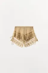 Shorts de tiro medio con cintura elástica, confeccionados en tejido con superposición de volantes, bordados florales y detalles de abalorios. Presenta tiras laterales ajustables con lazada.