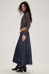 Falda midi de denim azul oscuro con costuras a la vista en contraste. Presenta un diseño de corte recto con paneles verticales y un cinturón de gamuza en tono tostado con hebilla metálica.