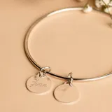 Brazalete tipo esclava de alambre redondo en plata 925, con dos medallas circulares colgantes, una de ellas con grabado personalizado.