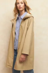 Piloto beige de manga larga con capucha, bolsillos de solapa y botones metálicos.