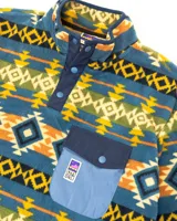 Buzo polar de cuello alto con cierre frontal de botones a presión, confeccionado en fleece sintético. Presenta un estampado geométrico multicolor con predominancia de tonos azules, amarillos y verdes. Incluye un bolsillo frontal tipo cargo con solapa y cierre de botón, además de bolsillos laterales ocultos.