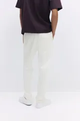 Jogger color blanco hueso en tejido suave de mezcla de algodón, con pliegue cosido en la parte delantera. Presenta cierre decorativo, cintura elástica con cordón ajustable, bolsillos laterales y un bolsillo insertado en la parte trasera. Corte estándar.