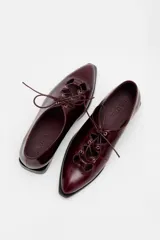 Zapato acordonado de cuero color bordó, con punta fina y diseño estilo oxford. Presenta cordones al tono y detalles de ojales metálicos dorados.