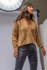 Saco tejido de punto color camel, con diseño de trenzas verticales, escote en V y cierre frontal con botones al tono. Presenta mangas largas con puños acanalados y un corte a la cintura.