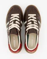 Championes Coolway modelo Kiro Espresso Pace de estilo retro, fabricados principalmente en gamuza color marrón. Presentan doble franja lateral en color blanco con bordes verdes, cordones claros, detalle rojo en la parte trasera del talón y suela de goma translúcida.