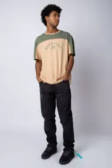 Remera de algodón con diseño color block, combinando tonos beige y verde militar. Presenta cuello redondo y estampa frontal con la frase 'Pan y Vino' y el logo 'VCP Argentina'.