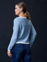 Cardigan de tejido tweed celeste y blanco, con escote redondo, cierre frontal con botones metálicos dorados y bolsillos simulados en el frente.