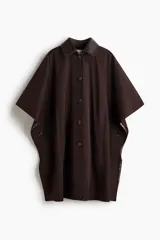 Abrigo oversized de sarga color marrón con cuello de cuero sintético. Modelo con botones en el frente, bolsillos laterales discretos, mangas tipo capa y aberturas laterales con botón.