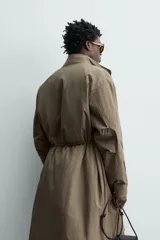 Parka relaxed fit de tejido técnico ligero, color verde militar, con cuello subido, manga larga y bolsillos de plastrón con solapa en la cadera. Cuenta con cintura ajustable con cordones y cierre frontal con cremallera oculta por solapa con botones a presión.