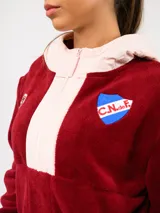Buzo de micropolar color bordó con capucha, cierre frontal parcial y detalles en color crema. Presenta el logo de Umbro y el escudo del Club Nacional de Football bordados en el frente.