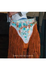 Cartera bandolera de cuero en color marrón terracota y blanco, con diseño de flecos largos y solapa frontal pintada a mano con detalles en tonos turquesa y dorado.