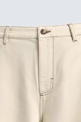 Pantalón de algodón color beige claro, de corte recto (regular fit), con pespuntes en hilo contrastante oscuro. Presenta bolsillos delanteros y bolsillos traseros de parche.