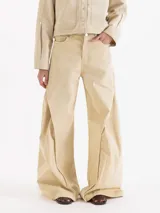 Pantalón wide leg de gabardina color beige, de tiro medio, con recortes diagonales y pespuntes a la vista que aportan volumen, bolsillos delanteros y pasadores en la cintura.