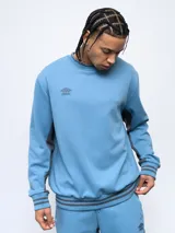 Buzo negro de corte clásico con cuello redondo, puños y ruedo acanalados con doble línea blanca. Logo de Umbro bordado en el pecho. Mangas con paneles laterales en gris. Confeccionado en algodón y poliéster.